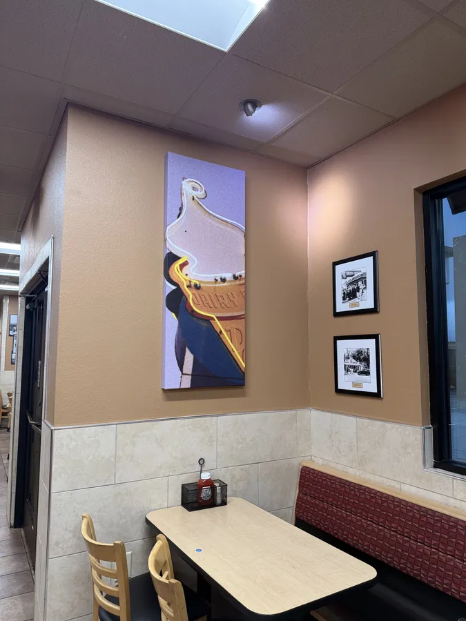A two-top table under a tall painted Dairy Queen cone and framed black-and-white photographs.