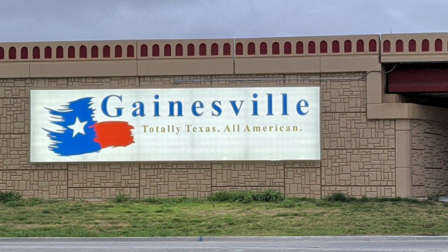 The lit "Gainesville — Totally Texas. All American." sign on the I-35 overpass wall at California Street.