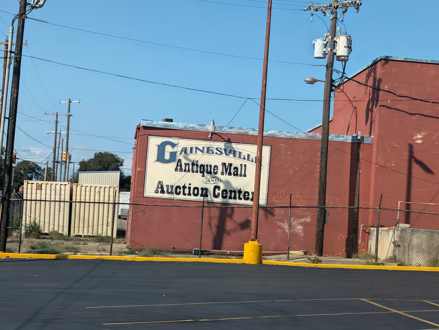 A painted sign for the Gainesville Antique Mall and Auction Center covers a red brick wall.