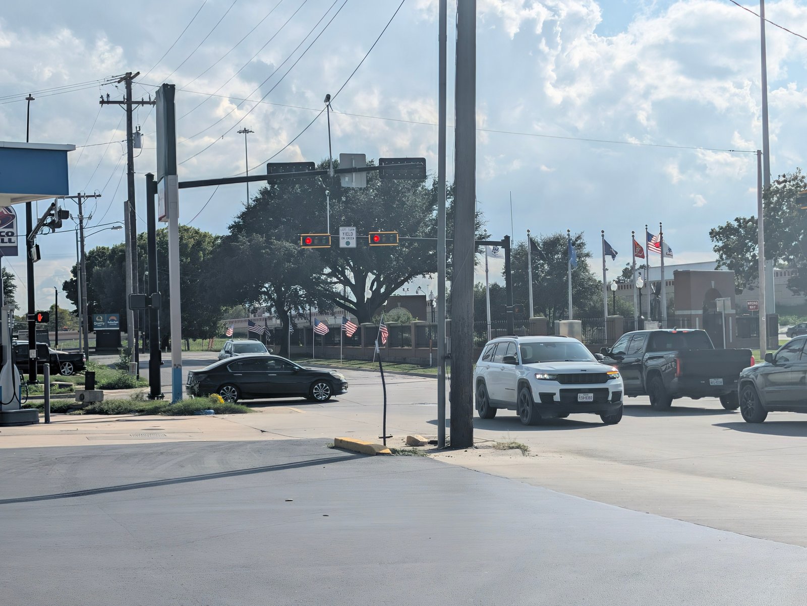 Afternoon traffic waits at a signal near I-35, with American flags along the roadside.