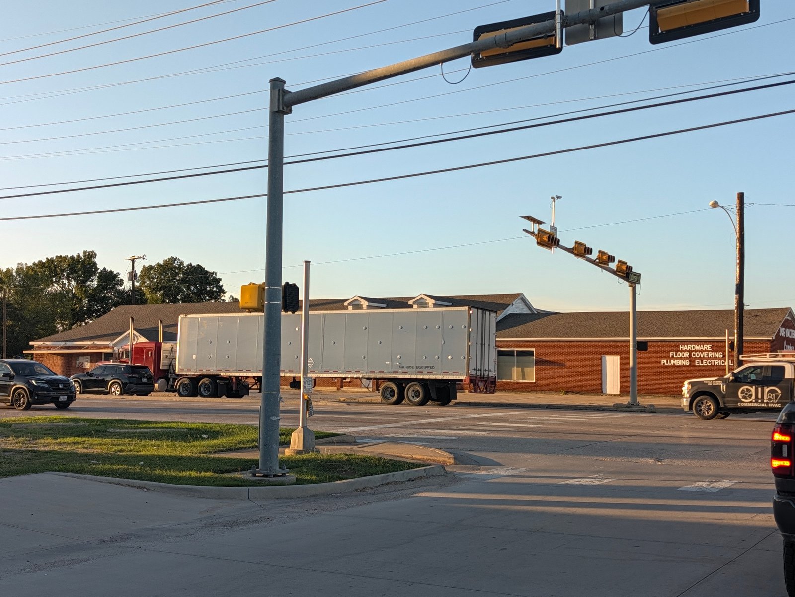A truck passes Joe Walter Lumber, whose brick wall advertises hardware, floor covering, plumbing and electrical supplies.