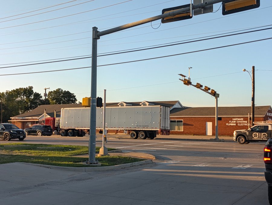A truck passes Joe Walter Lumber, whose brick wall advertises hardware, floor covering, plumbing and electrical supplies.